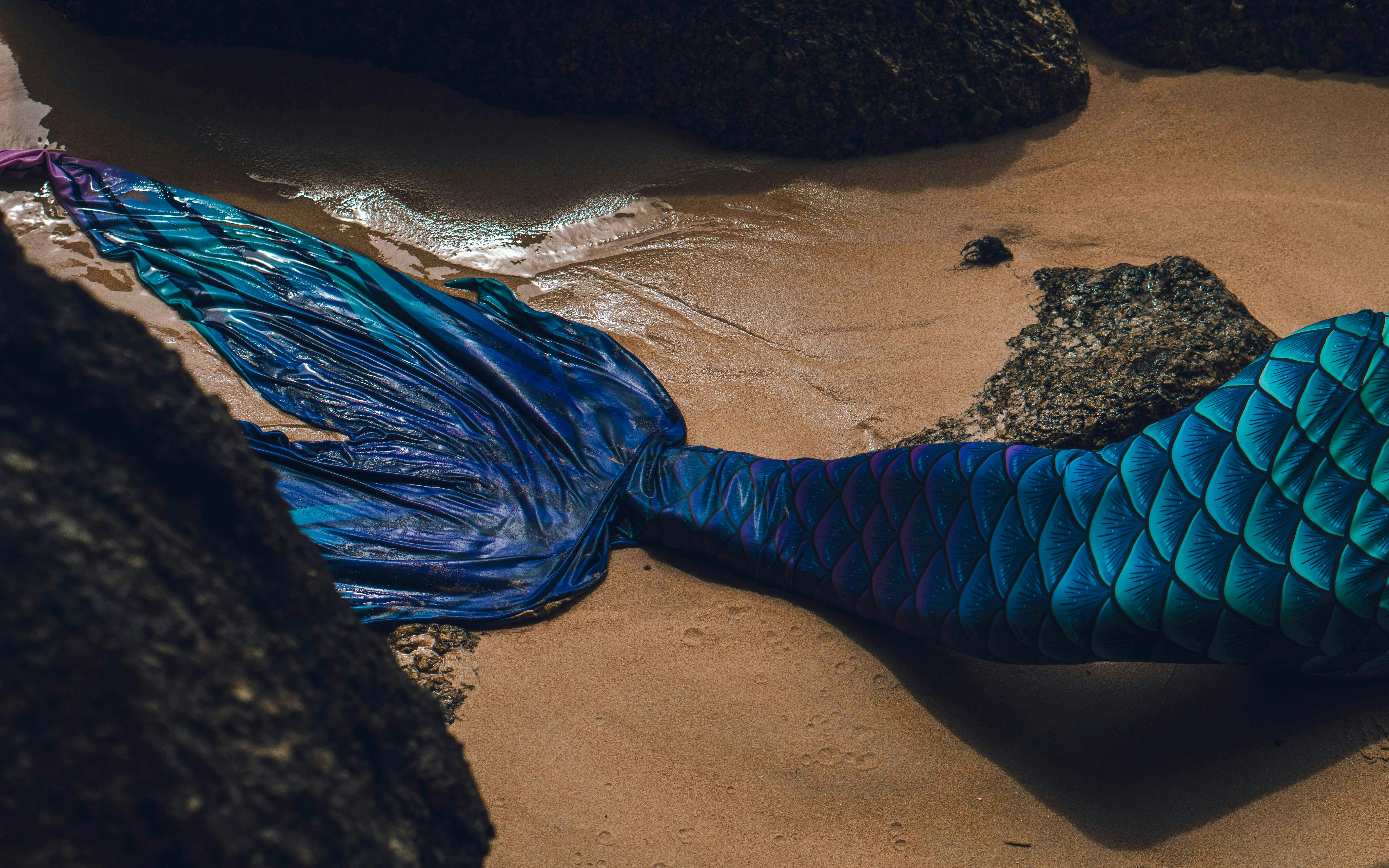 Mermaid tail costume on sandy beach near rocks.