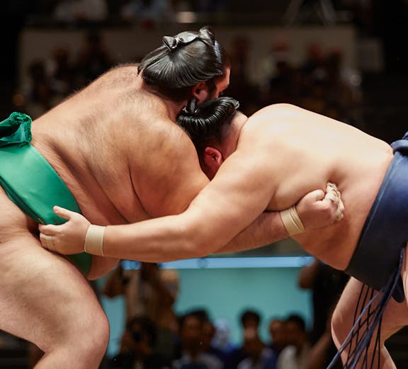 Sumo wrestlers grappling in a match at a tournament in Japan.