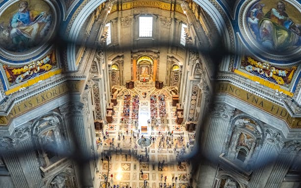 Interior view from the dome of Saint Peter's Basilica, Vatican City, showing ornate architecture and visitors below.