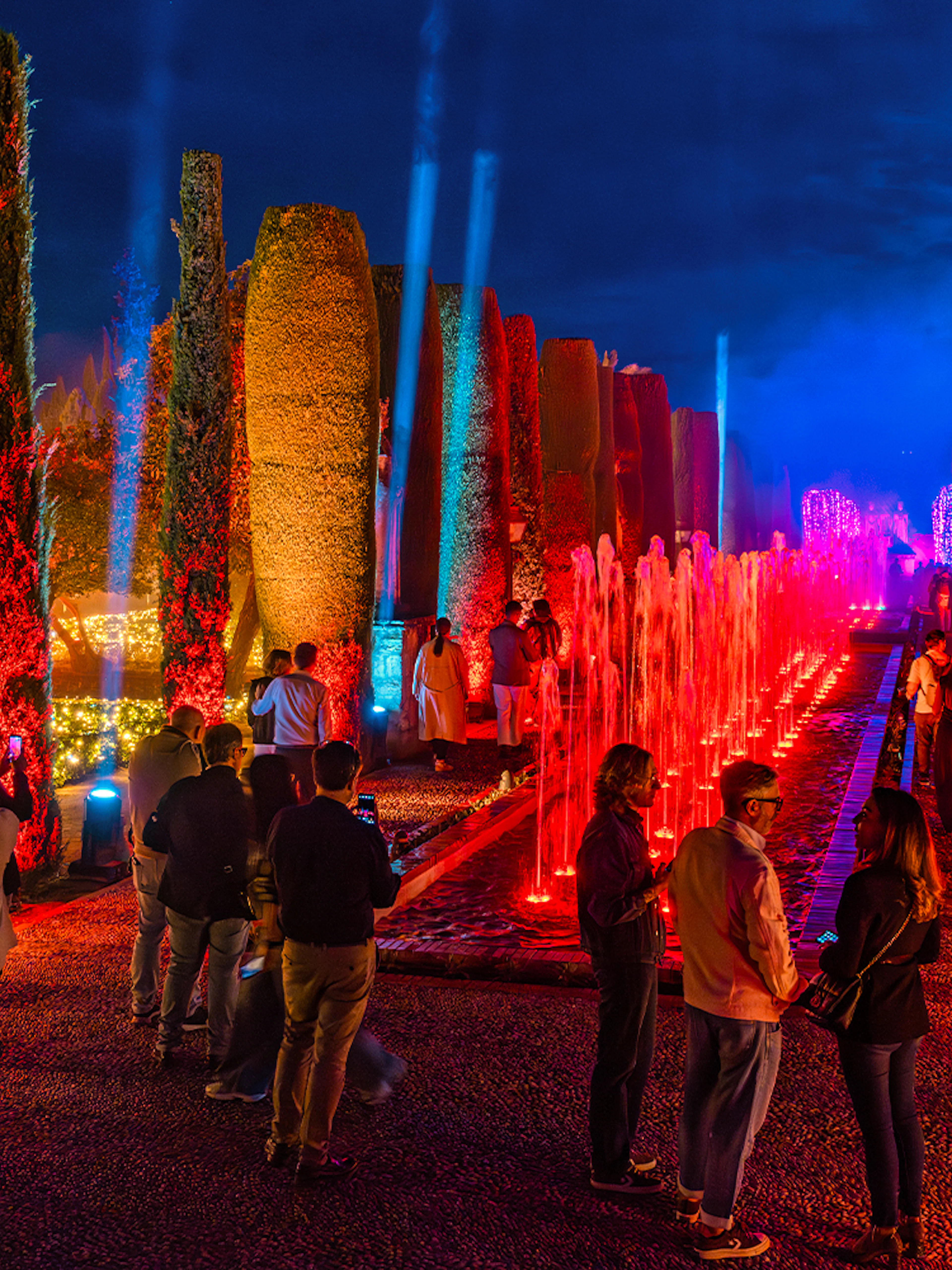 Alcazar of Cordoba garden illuminated at night with colorful lights and fountains.