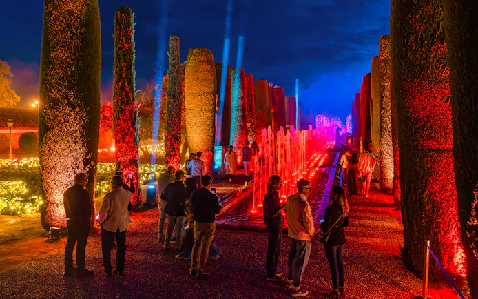 Alcazar of Cordoba garden illuminated at night with colorful lights and fountains.