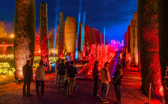 Alcazar of Cordoba garden illuminated at night with colorful lights and fountains.