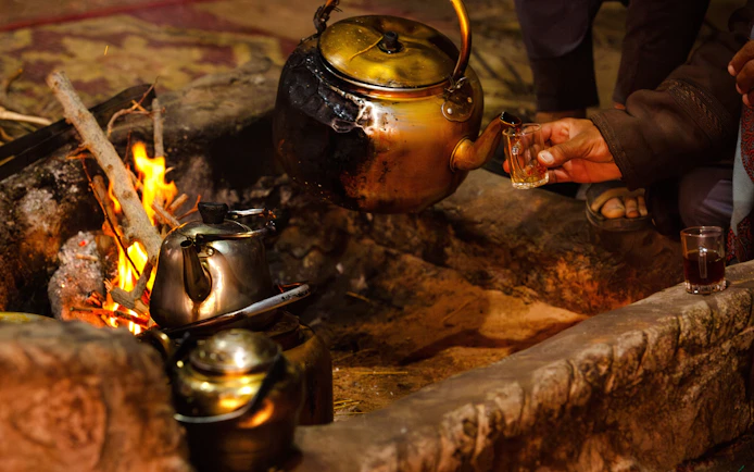 Bedouin tea being poured from a brass kettle over an open fire.