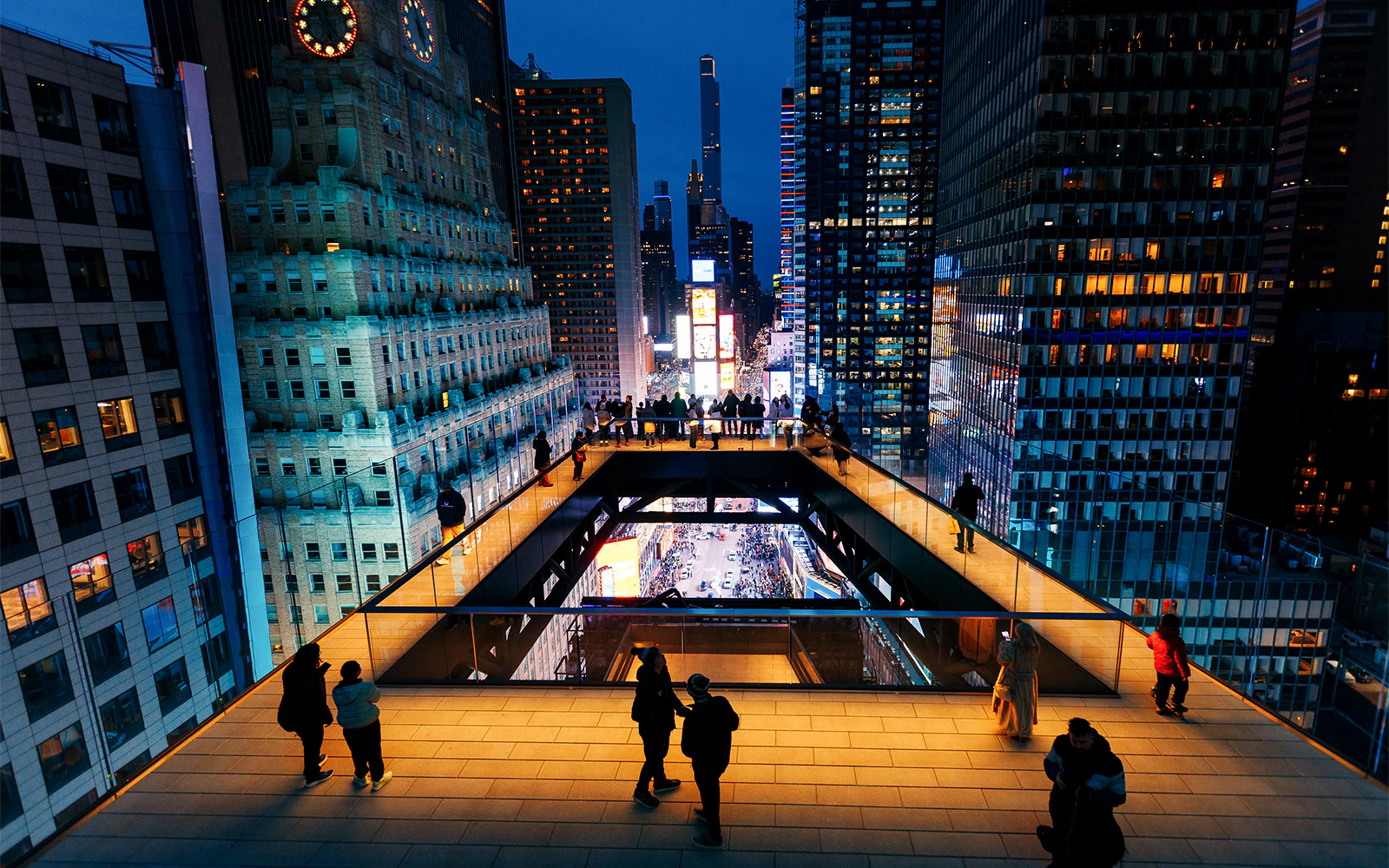 Visitors on the One Times Square Skywalk overlooking illuminated cityscape at night.