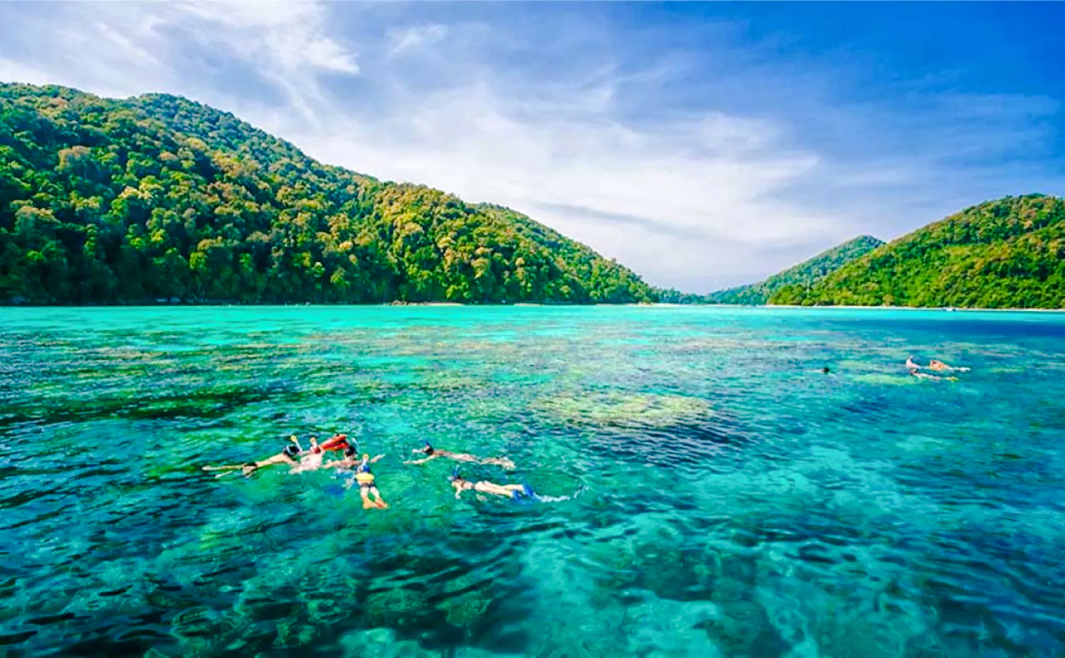 Snorkelers exploring clear waters near Surin Islands, Krabi, with lush hills in the background.