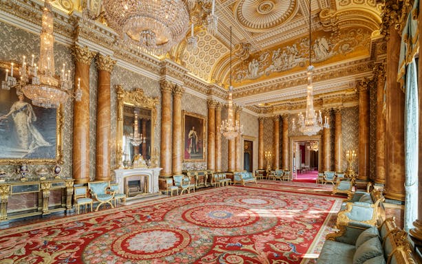 Buckingham Palace State Room with ornate chandeliers, gilded columns, and luxurious red carpet.