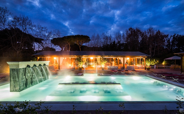Outdoor thermal pool at QC Terme Roma with illuminated spa area at dusk.