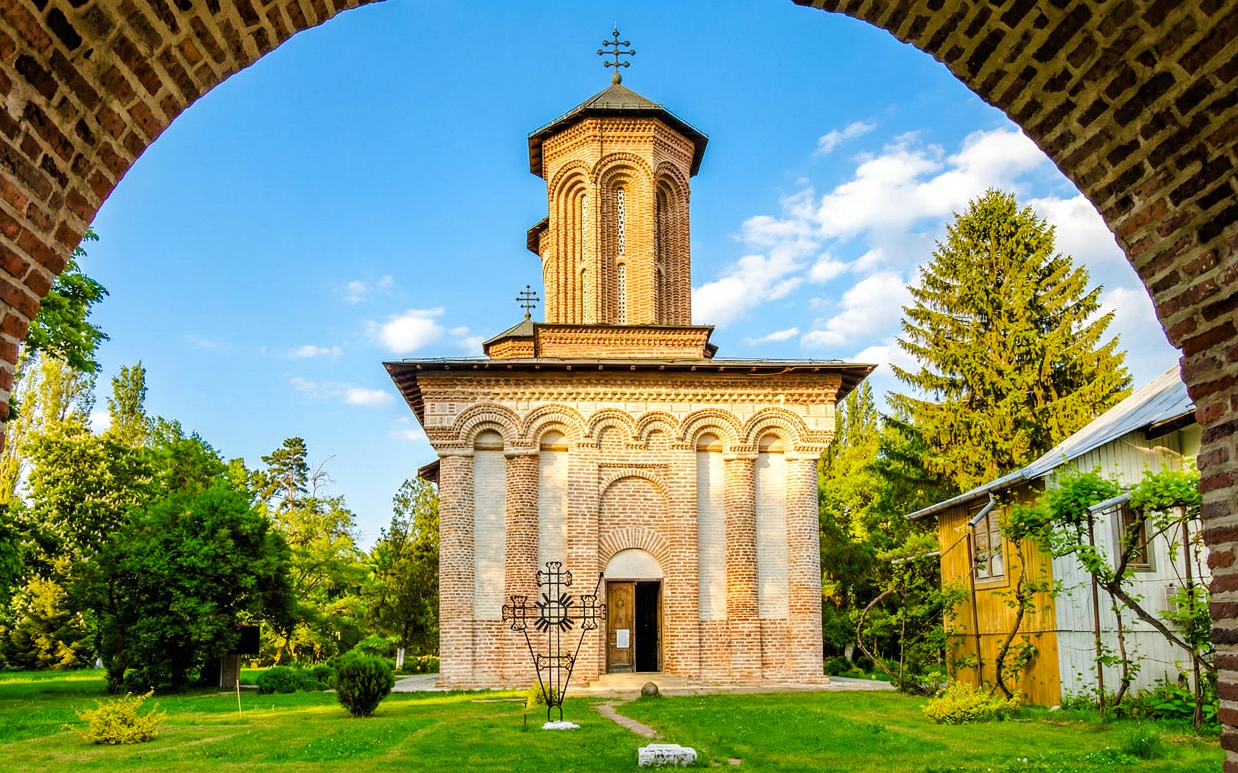 Snagov Monastery brick facade with cross, surrounded by greenery and trees.