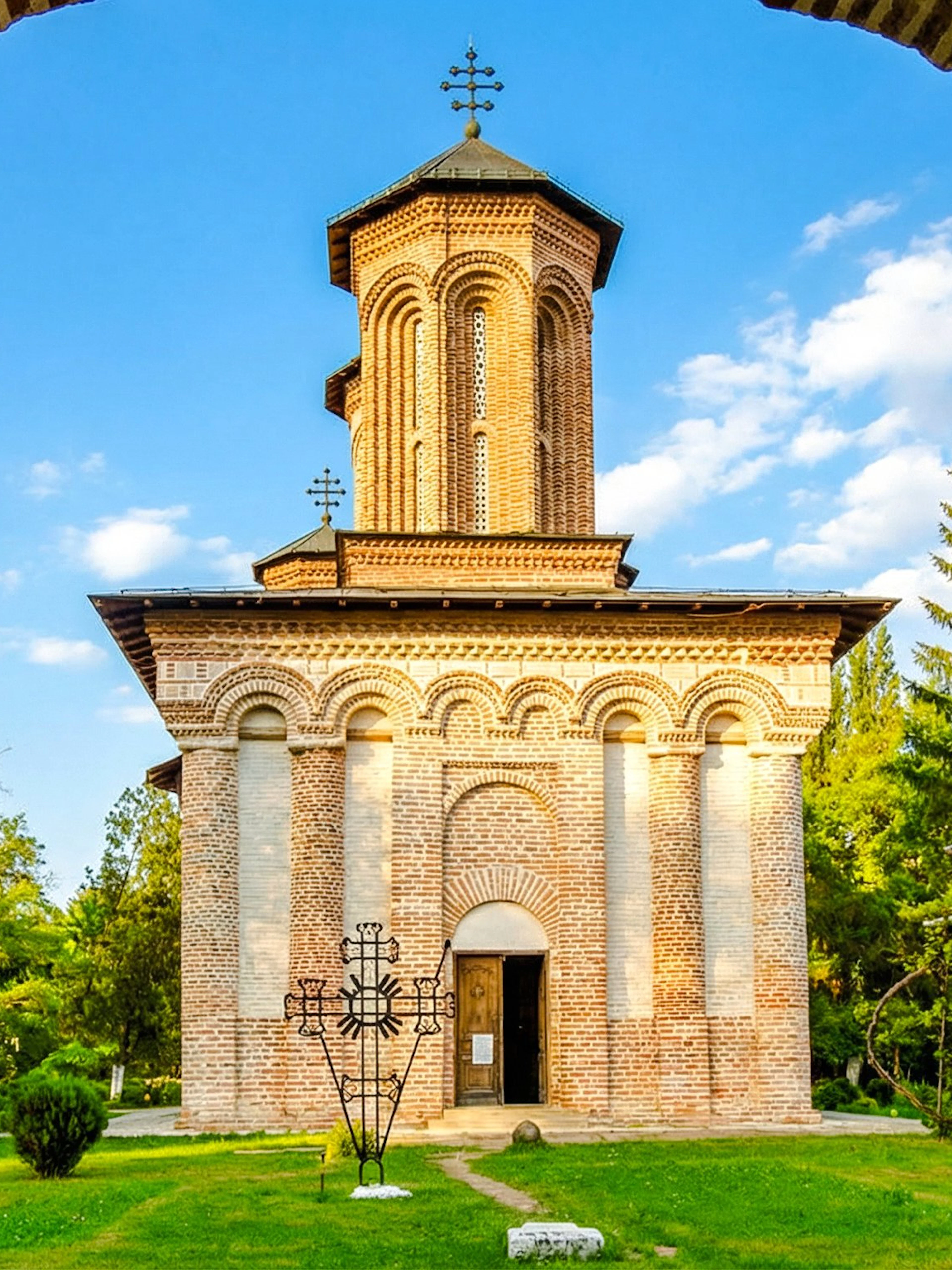 Snagov Monastery brick facade with cross, surrounded by greenery and trees.