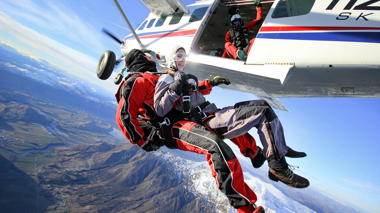 Tandem skydive over Queenstown with snowy mountains and valleys below.