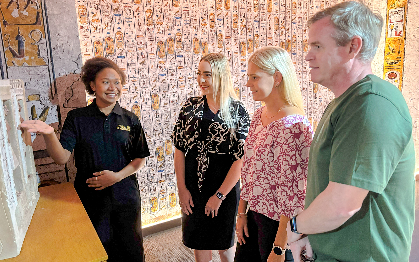 Tour guide explains an exhibit to visitors in an Egyptian-themed museum.