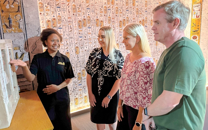 Tour guide explains an exhibit to visitors in an Egyptian-themed museum.