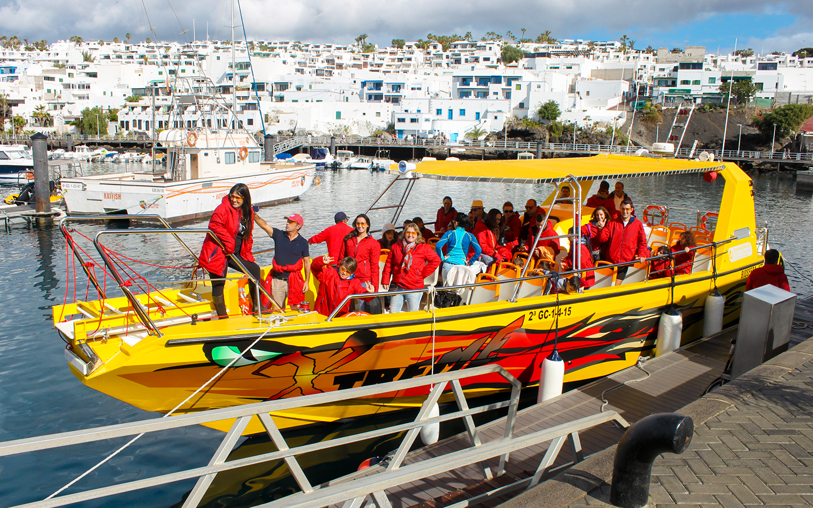 Tourists in red jackets boarding a yellow boat at a port for a dolphin watching tour.
