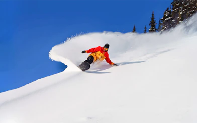 Snowboarder carving down a snowy slope with Ikon Pass, global ski pass.