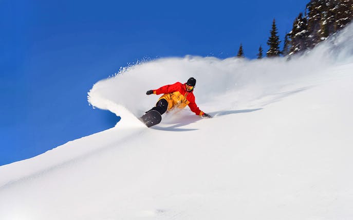 Snowboarder carving down a snowy slope with Ikon Pass, global ski pass.