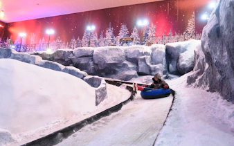 Person tubing down snowy slope at Genting Highlands Snow World Theme Park.