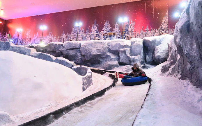 Person tubing down snowy slope at Genting Highlands Snow World Theme Park.