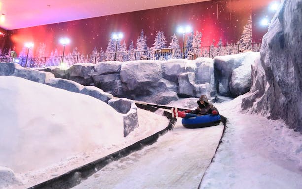 Person tubing down snowy slope at Genting Highlands Snow World Theme Park.