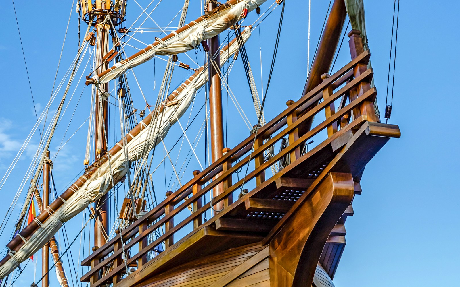 Replica wooden ship bow view with intricate carvings, docked at a historical port in Amsterdam.