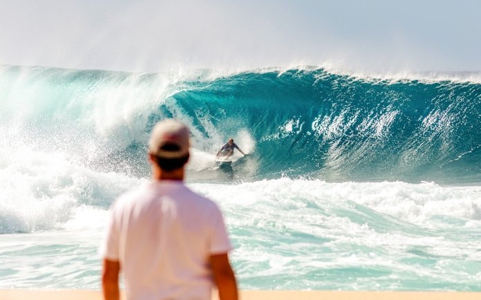 Tourist watching a surfer ride a large wave at the beach.