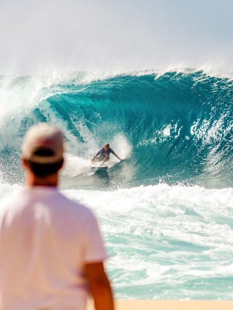 Tourist watching a surfer ride a large wave at the beach.