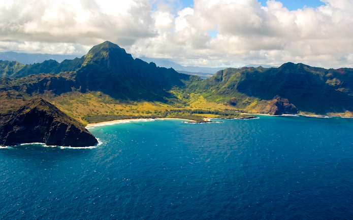 Aerial view of Kauai coastline with lush mountains and blue ocean.