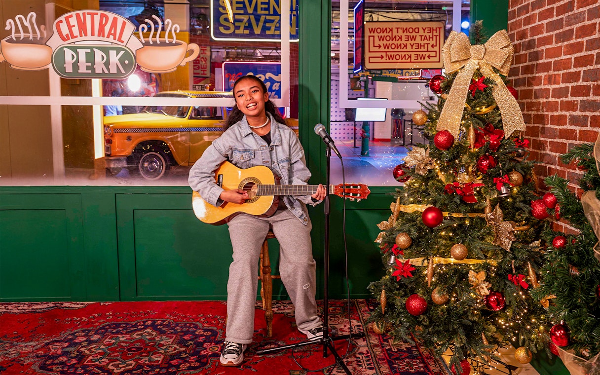 Person playing guitar at Central Perk set with Christmas tree, The FRIENDS™ Experience.