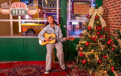 Person playing guitar at Central Perk set with Christmas tree, The FRIENDS™ Experience.