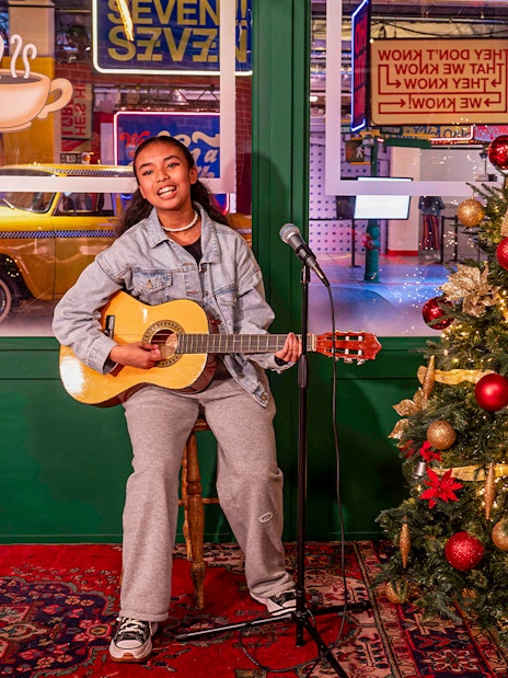 Person playing guitar at Central Perk set with Christmas tree, The FRIENDS™ Experience.