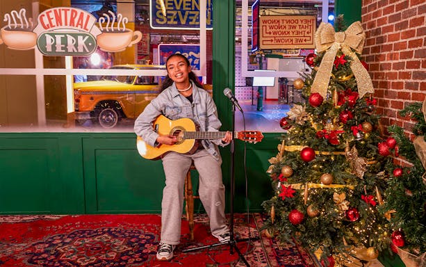 Person playing guitar at Central Perk set with Christmas tree, The FRIENDS™ Experience.