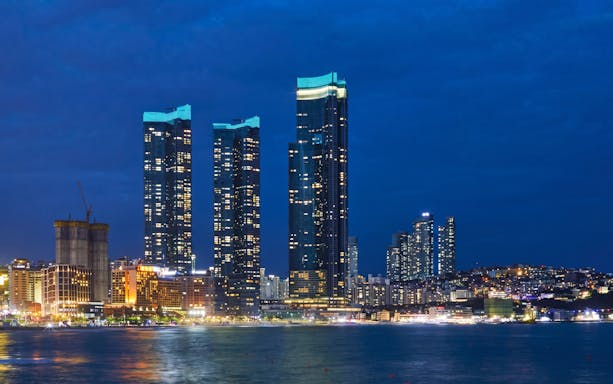 Busan skyline at night with illuminated skyscrapers near the waterfront.