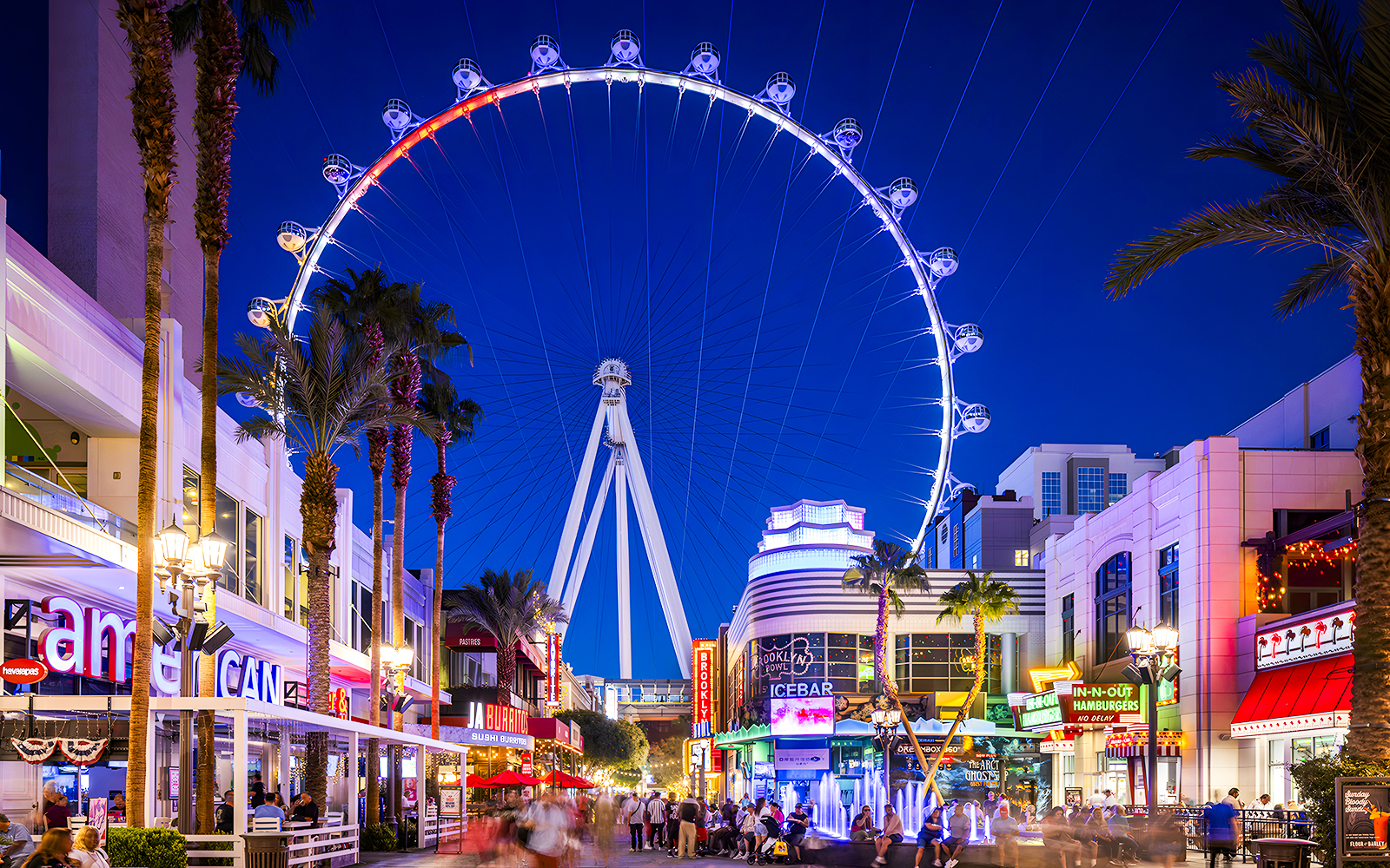 High Roller Wheel illuminated at night, Las Vegas promenade bustling with visitors.