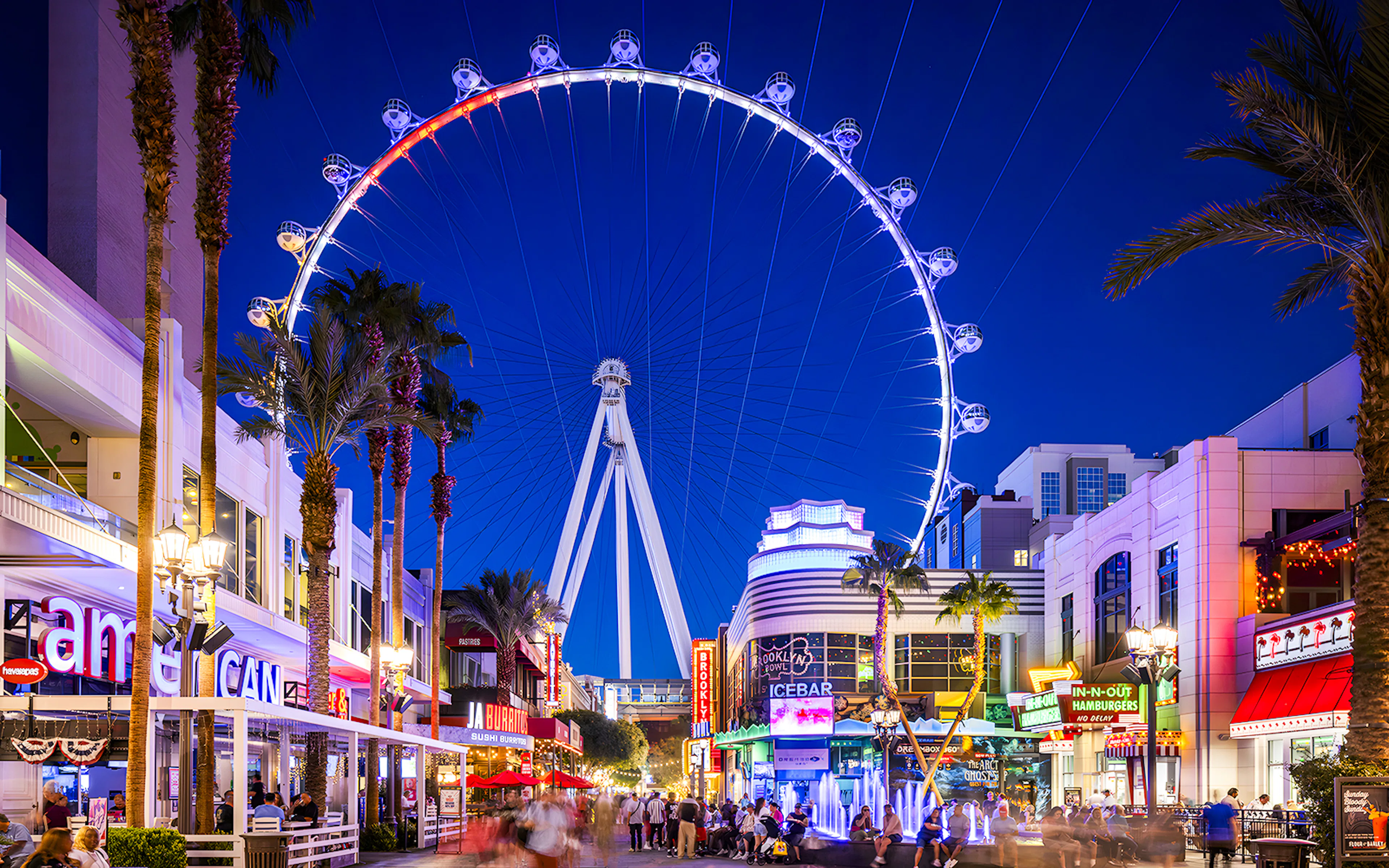 High Roller Wheel illuminated at night, Las Vegas promenade bustling with visitors.