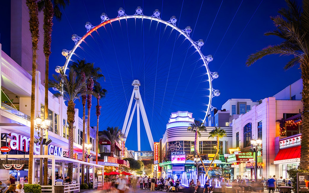 High Roller Wheel illuminated at night, Las Vegas promenade bustling with visitors.