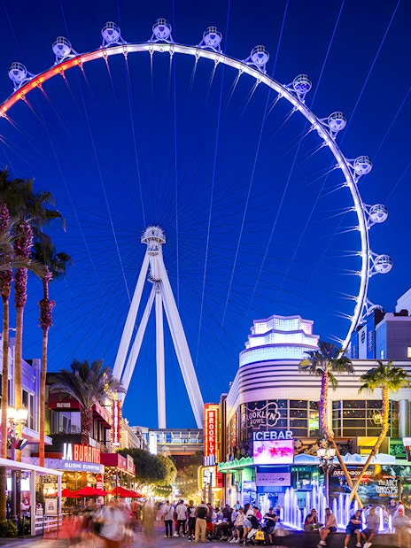 High Roller Wheel illuminated at night, Las Vegas promenade bustling with visitors.