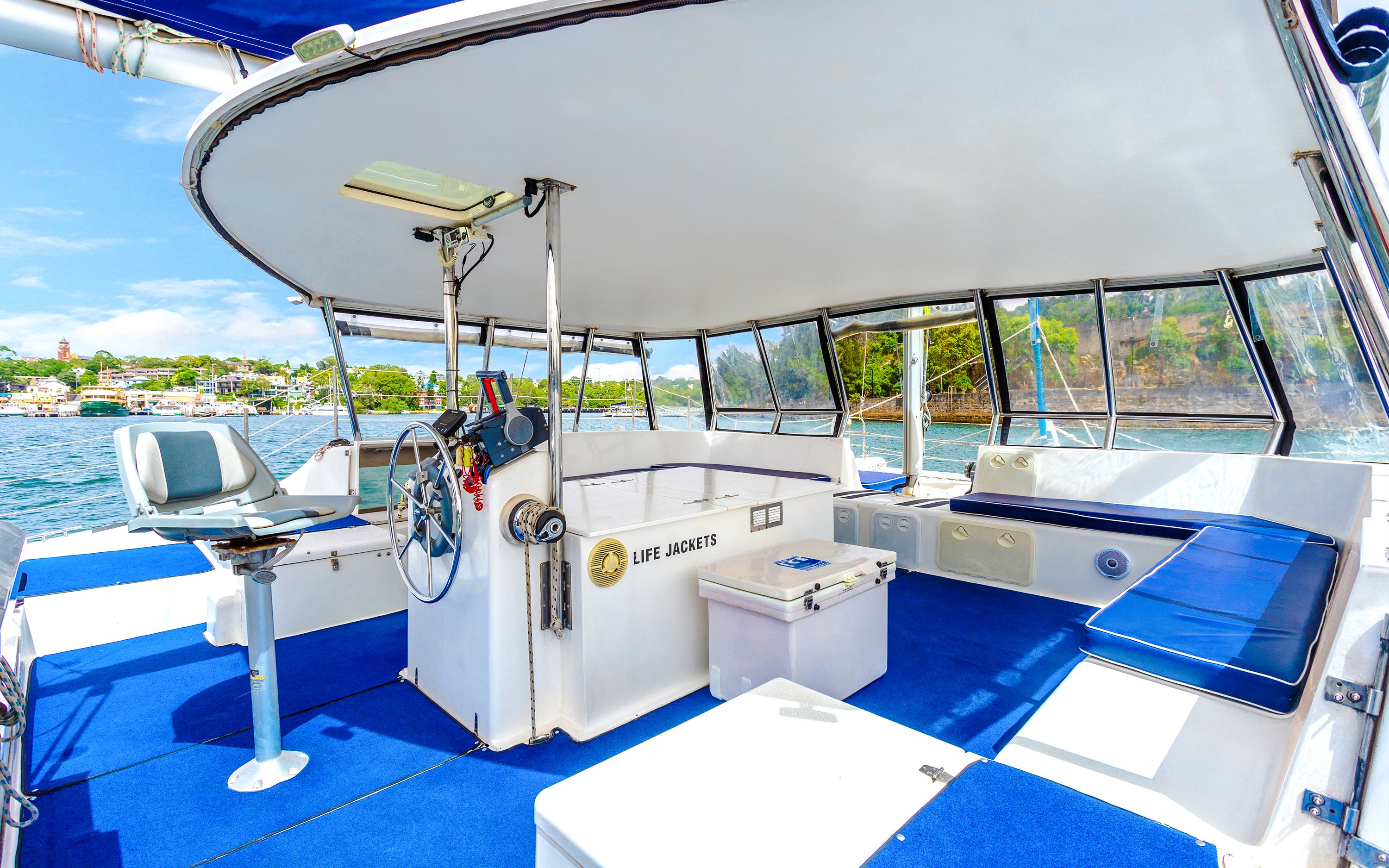 Luxury cruise boat interior with seating and steering wheel, Sydney Harbour in the background.