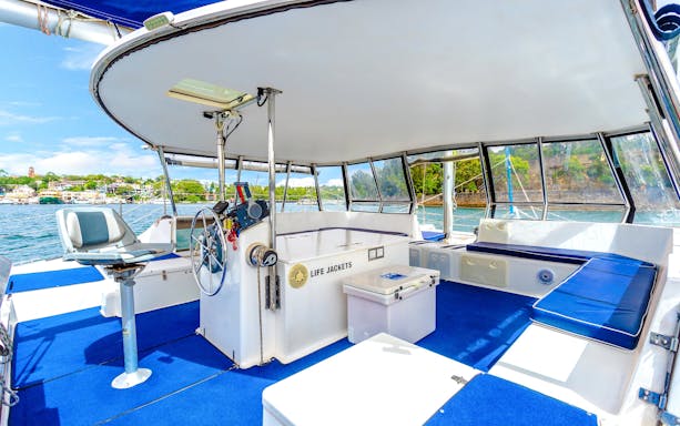 Luxury cruise boat interior with seating and steering wheel, Sydney Harbour in the background.