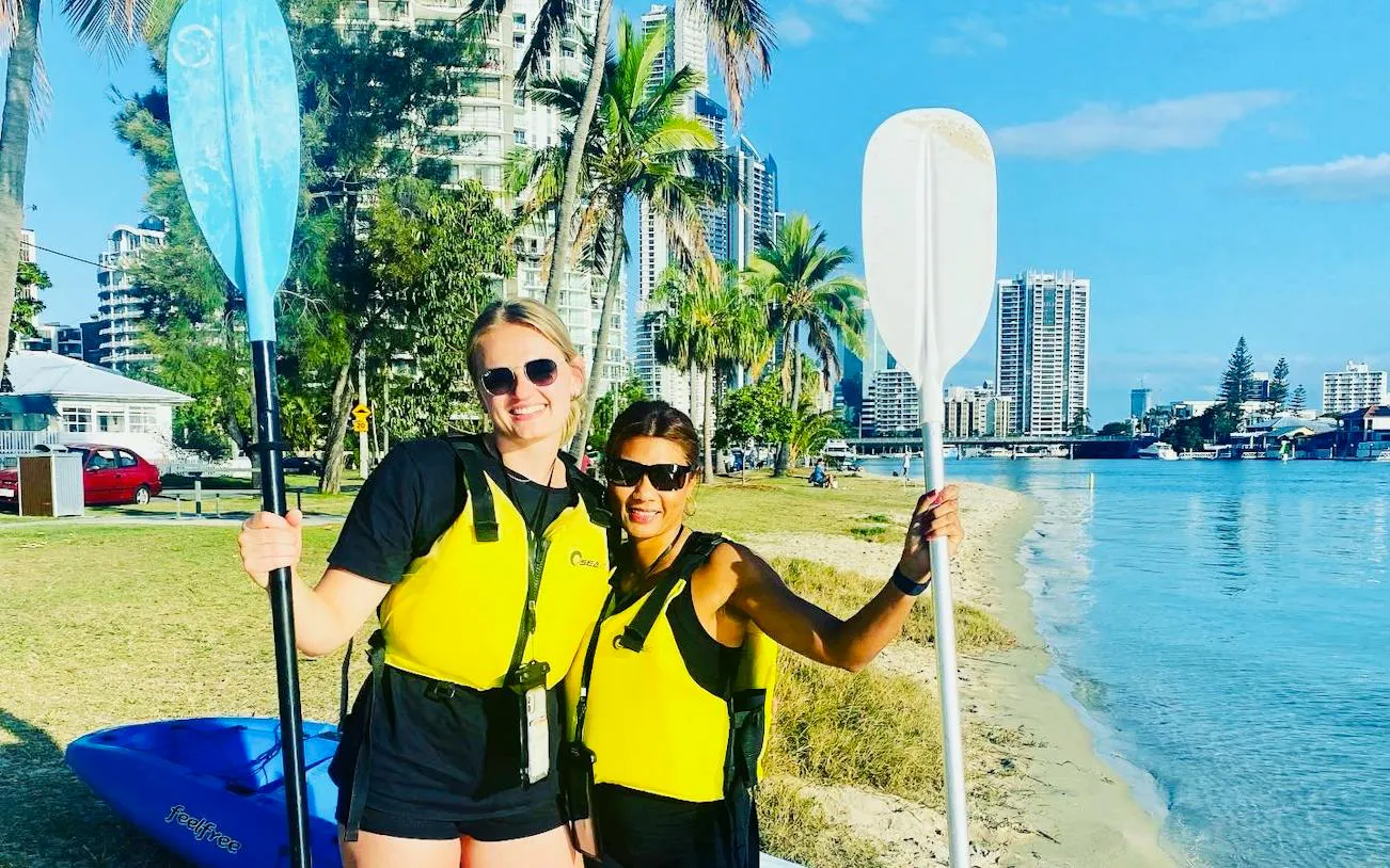 Surfers Paradise kayakers on Gold Coast beach with city skyline in background.