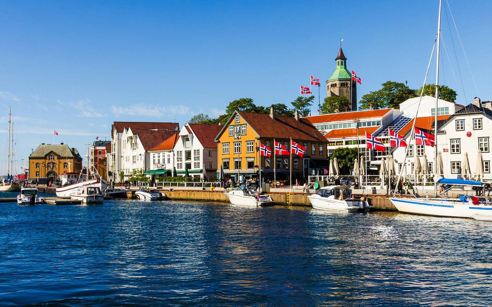Boats docked along Skagenkaien waterfront in Stavanger, Norway, with colorful buildings and flags.