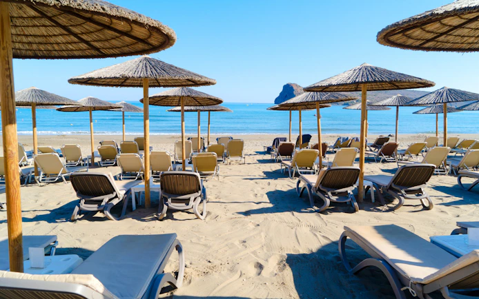 Sun loungers and umbrellas on Agia Marina beach, Crete, Greece, with sea view.
