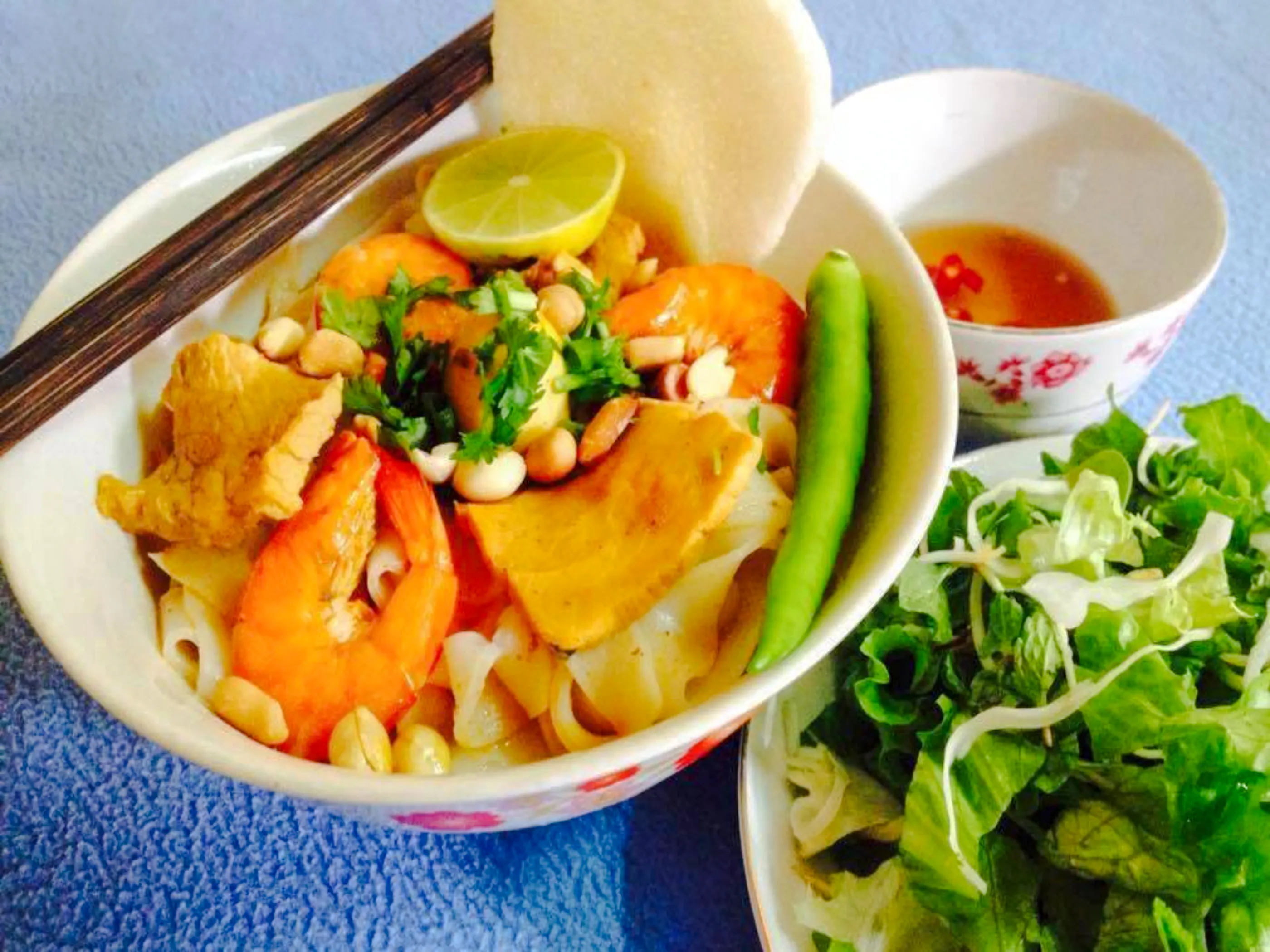 Bowl of Vietnamese noodles with shrimp, pork, peanuts, and herbs, served with salad and dipping sauce in Da Nang.