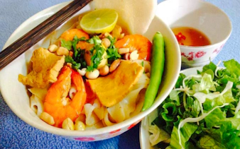 Bowl of Vietnamese noodles with shrimp, pork, peanuts, and herbs, served with salad and dipping sauce in Da Nang.