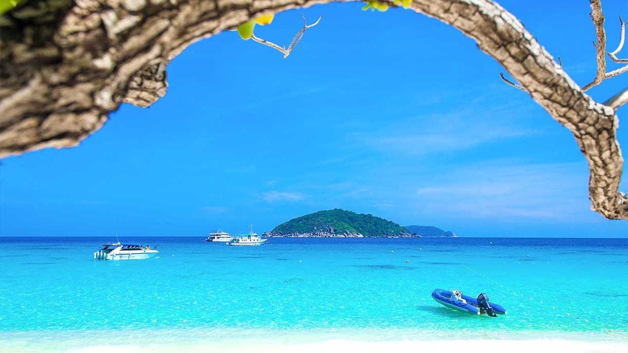 Boats on turquoise water near Similan Islands with lush island in the background.