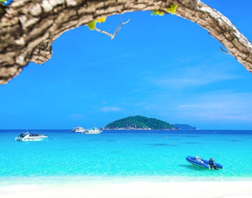 Boats on turquoise water near Similan Islands with lush island in the background.