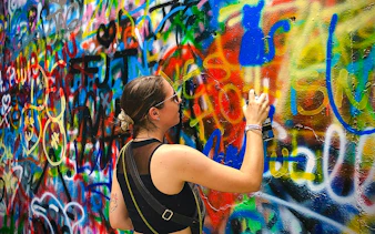 Guest spray painting colorful graffiti on a wall during Medellin Comuna tour.