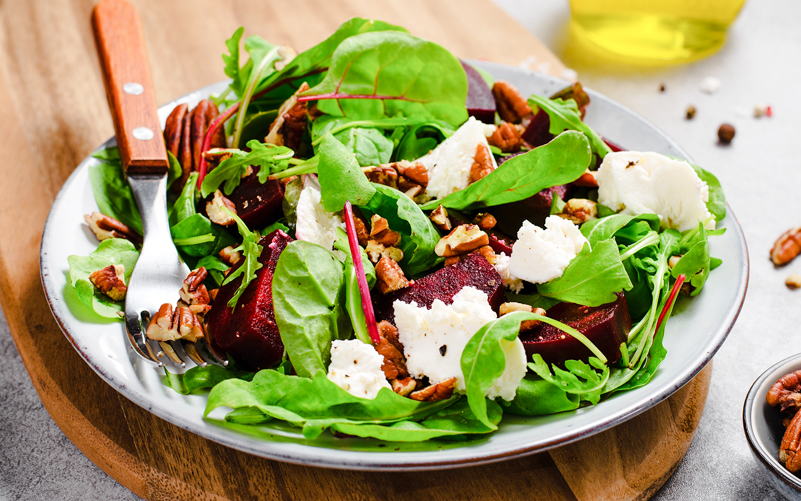 Goat cheese salad with mixed greens, beets, and pecans on a white plate.