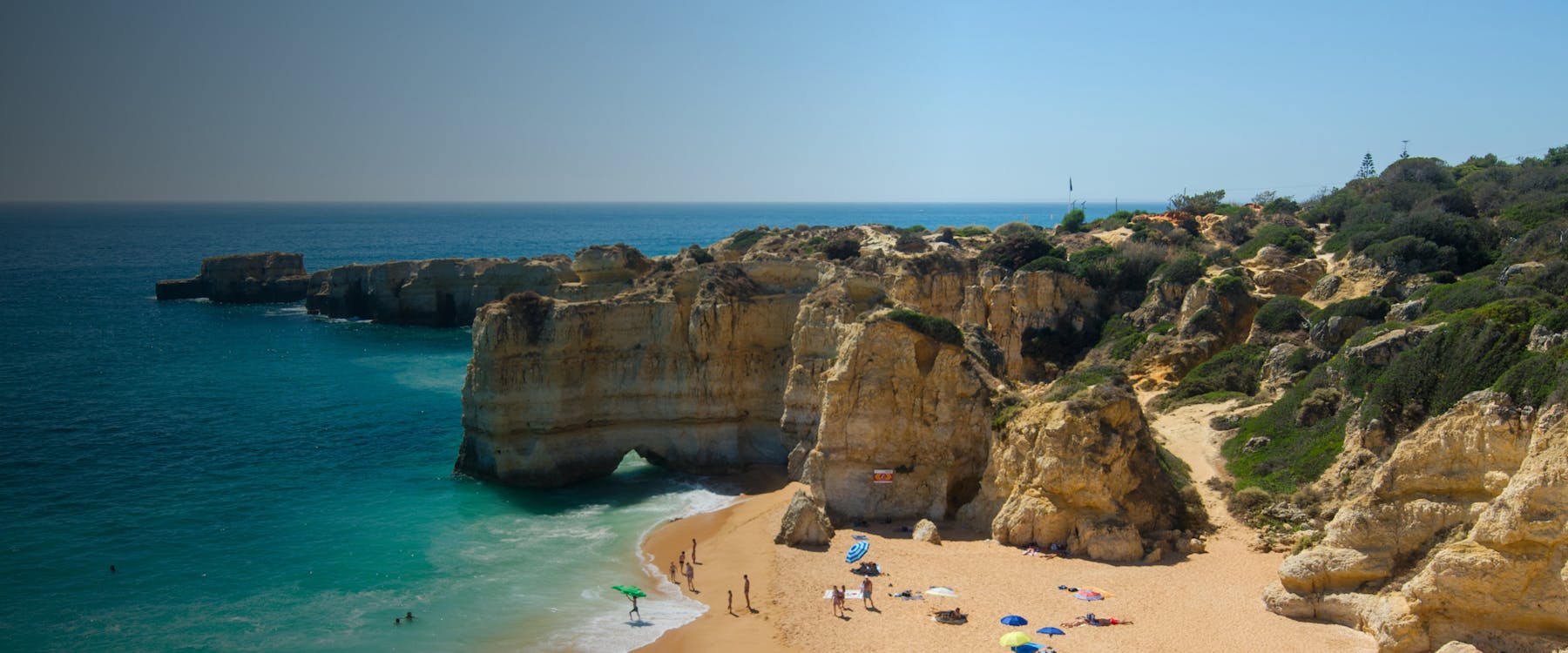 Cliffs and beach at Praia da Marinha, Faro, Portugal with people sunbathing and swimming.