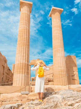 Traveler exploring ancient columns at the Acropolis of Lindos, Greece.