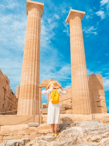 Traveler exploring ancient columns at the Acropolis of Lindos, Greece.