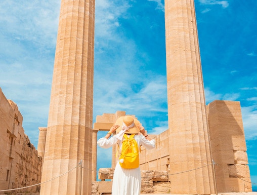 Traveler exploring ancient columns at the Acropolis of Lindos, Greece.